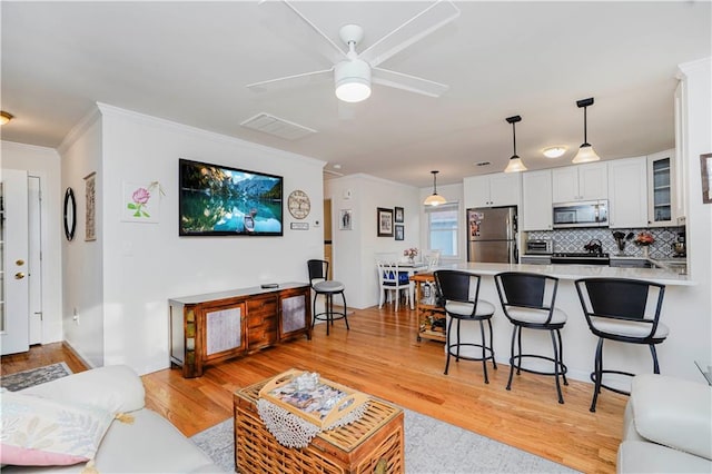 living area with a ceiling fan, visible vents, ornamental molding, and light wood-type flooring