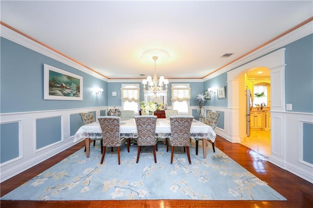 dining area featuring ornamental molding, arched walkways, wood finished floors, and a chandelier