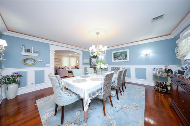 dining room with visible vents, crown molding, arched walkways, wood finished floors, and a notable chandelier