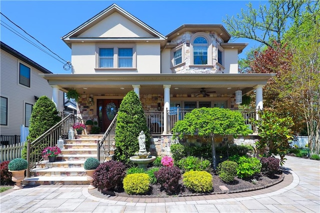 view of front facade with stone siding, ceiling fan, stucco siding, a porch, and stairway