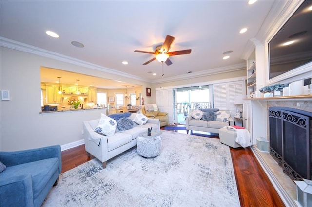 living room featuring a fireplace with raised hearth, ornamental molding, wood finished floors, and ceiling fan with notable chandelier
