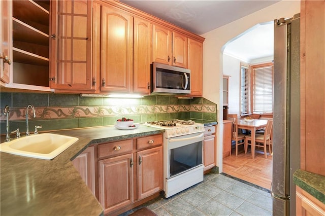 kitchen with white gas range, backsplash, dark countertops, a sink, and stainless steel microwave