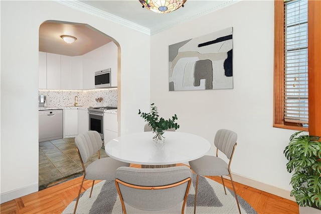 dining area with crown molding, arched walkways, baseboards, and light wood finished floors