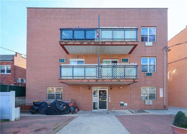 rear view of property with brick siding, a patio area, fence, and a balcony