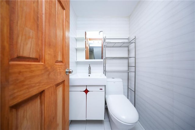 half bathroom featuring toilet, tile patterned floors, tile walls, and vanity