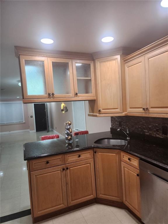 kitchen featuring a sink, dishwasher, dark stone countertops, tasteful backsplash, and glass insert cabinets