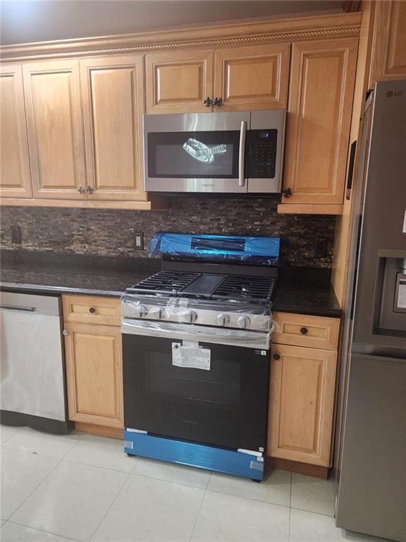 kitchen with light tile patterned floors, backsplash, dark countertops, and stainless steel appliances