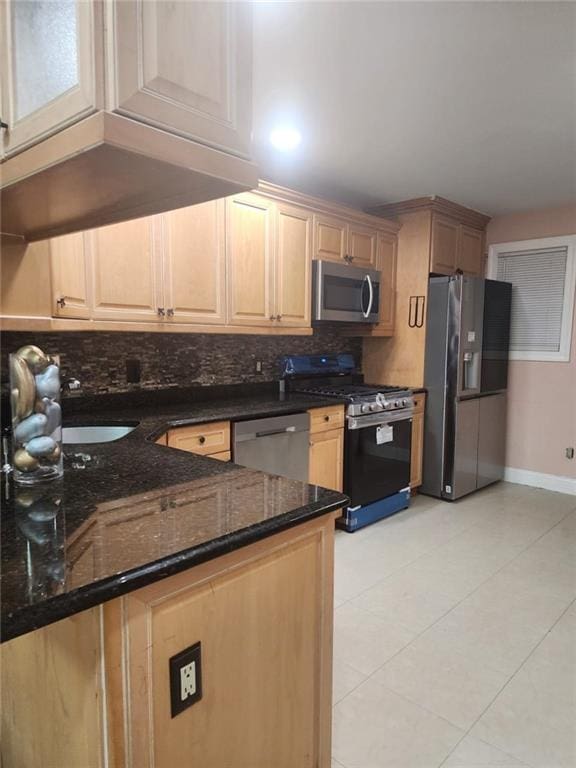 kitchen with appliances with stainless steel finishes, light brown cabinets, backsplash, and dark stone countertops