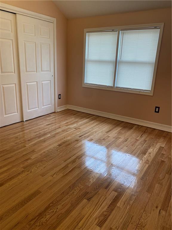 unfurnished bedroom featuring baseboards, wood finished floors, lofted ceiling, and a closet