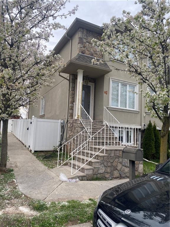 view of front of home featuring fence, stone siding, and stucco siding