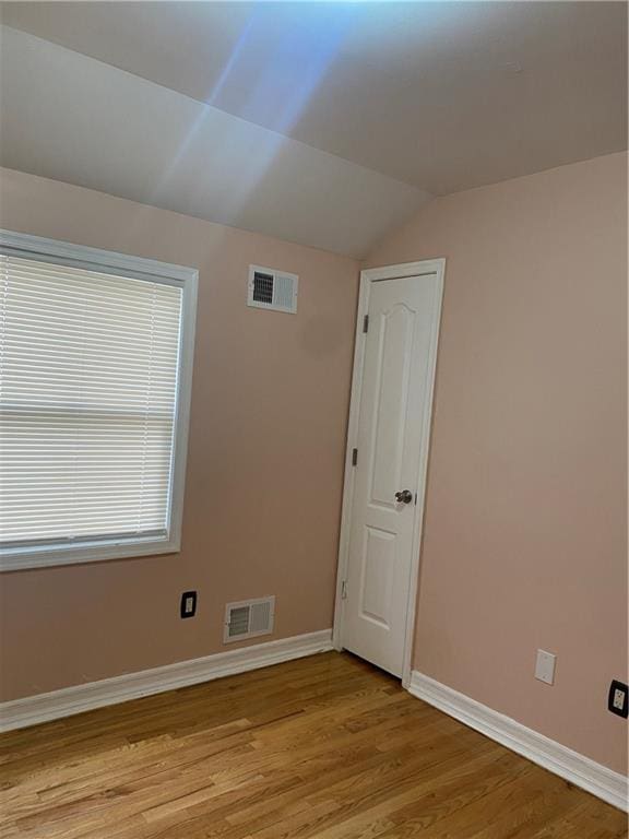 unfurnished room featuring baseboards, vaulted ceiling, light wood-style flooring, and visible vents