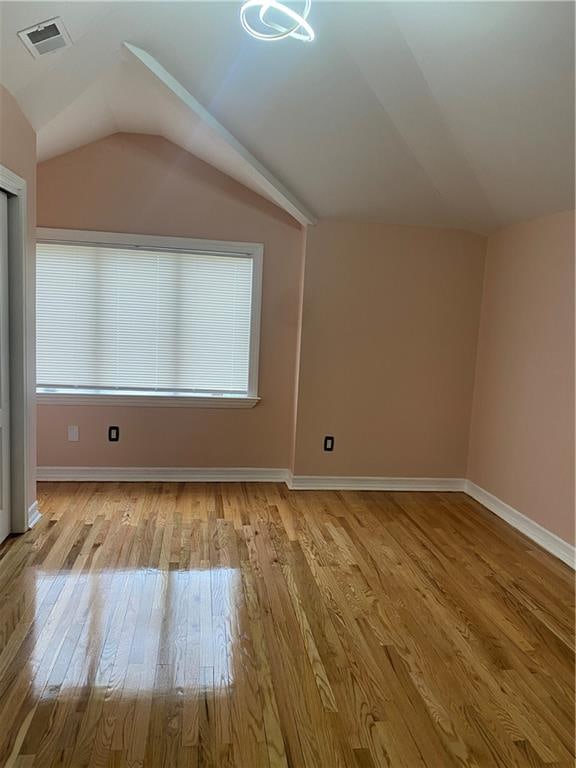 additional living space with baseboards, vaulted ceiling, wood finished floors, and visible vents