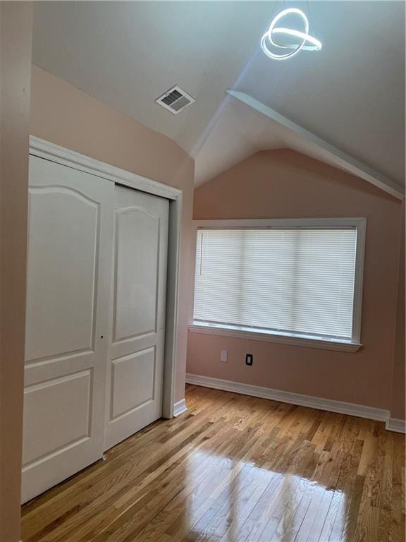 unfurnished bedroom with a closet, wood-type flooring, lofted ceiling, and visible vents