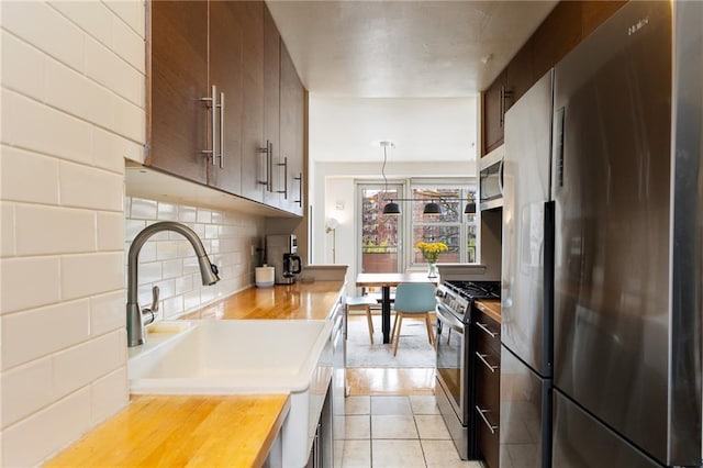 kitchen with decorative backsplash, appliances with stainless steel finishes, hanging light fixtures, a sink, and butcher block countertops