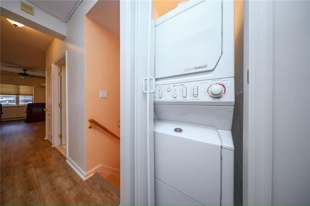 laundry room with laundry area, wood finished floors, baseboards, a baseboard radiator, and stacked washer / drying machine