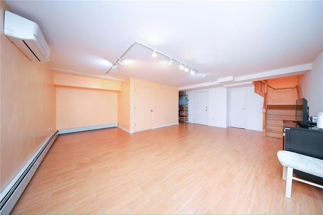 basement with a baseboard radiator, light wood finished floors, a wall unit AC, and rail lighting