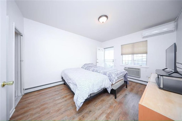 bedroom featuring a baseboard radiator, baseboard heating, a wall unit AC, an AC wall unit, and wood finished floors