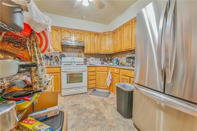 kitchen with freestanding refrigerator, white gas range oven, under cabinet range hood, stone finish floors, and decorative backsplash