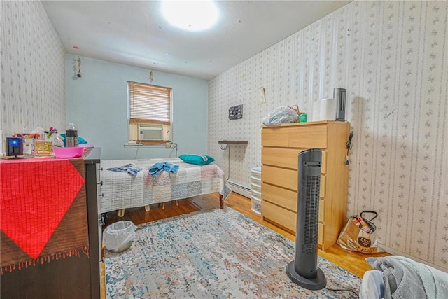 bedroom featuring wood finished floors, wallpapered walls, a baseboard radiator, and cooling unit