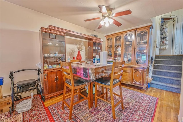 dining space with ceiling fan, light wood finished floors, and stairway