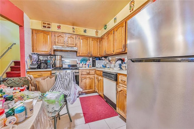 kitchen featuring appliances with stainless steel finishes, under cabinet range hood, light countertops, light tile patterned flooring, and brown cabinets