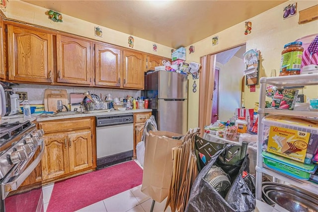kitchen featuring stainless steel appliances, light countertops, brown cabinets, and light tile patterned flooring