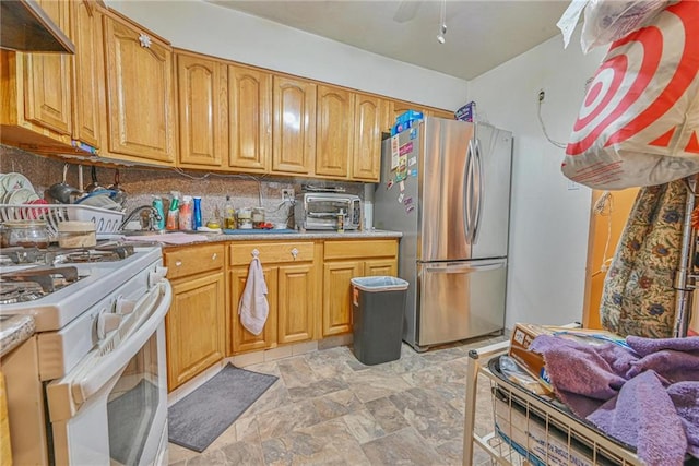 kitchen featuring freestanding refrigerator, gas range gas stove, under cabinet range hood, stone finish floors, and light countertops