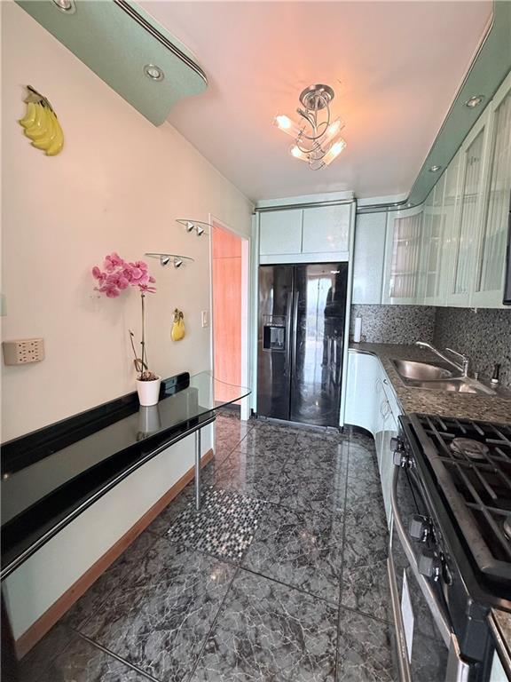 kitchen with backsplash, dark countertops, stainless steel gas range oven, a sink, and black refrigerator with ice dispenser