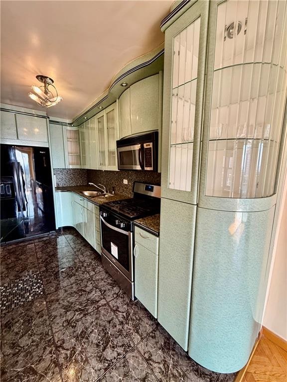 kitchen with dark countertops, appliances with stainless steel finishes, tasteful backsplash, a sink, and glass insert cabinets