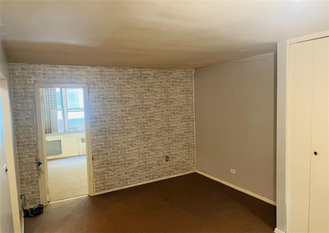 interior space featuring baseboards, dark carpet, and brick wall