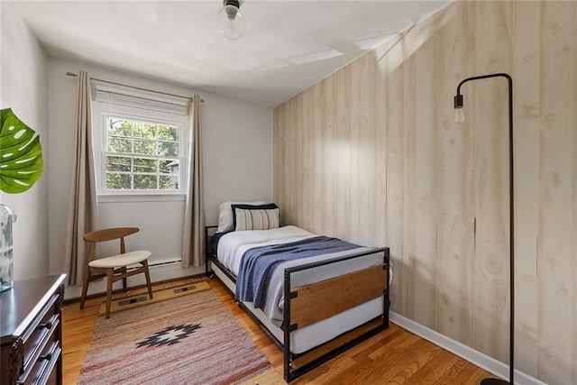 bedroom with wooden walls, a baseboard heating unit, and light wood-style floors
