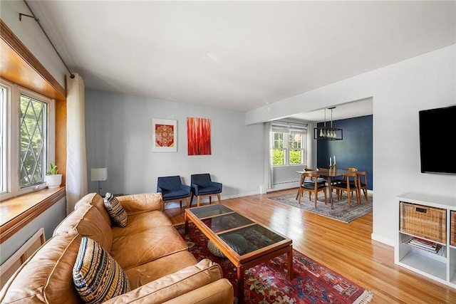 living room featuring light wood-style floors, baseboards, a baseboard radiator, and a notable chandelier