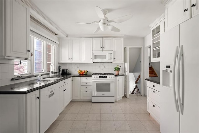 kitchen featuring backsplash, dark countertops, a sink, glass insert cabinets, and white appliances