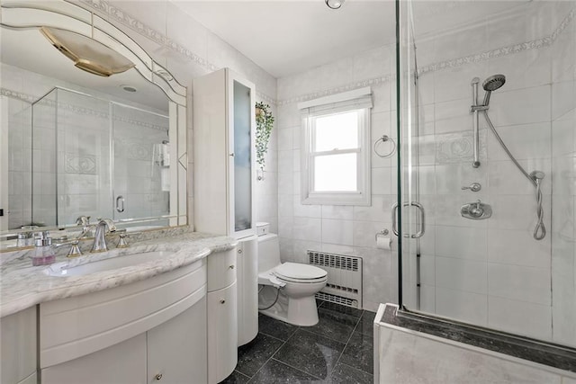 bathroom featuring vanity, toilet, radiator heating unit, tile walls, and a shower stall