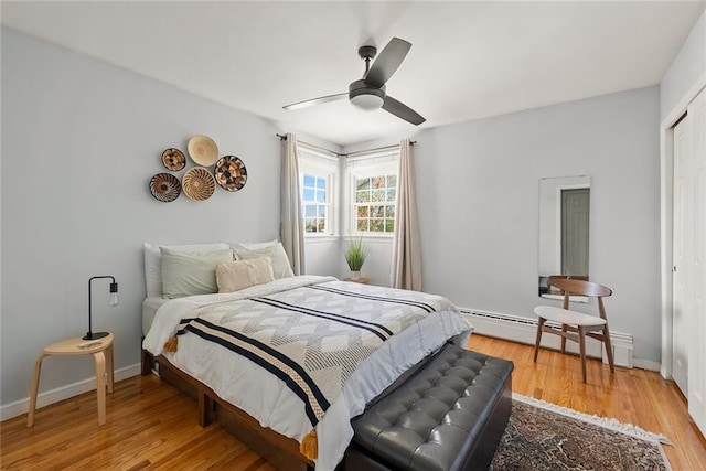 bedroom featuring ceiling fan, baseboards, a closet, a baseboard heating unit, and light wood-style floors