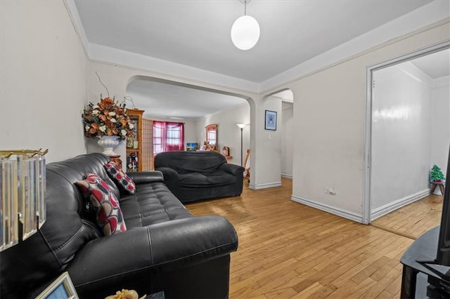 living area with arched walkways, baseboards, ornamental molding, and light wood-type flooring