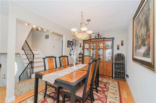 dining room featuring a textured ceiling, visible vents, light wood-type flooring, stairway, and a notable chandelier