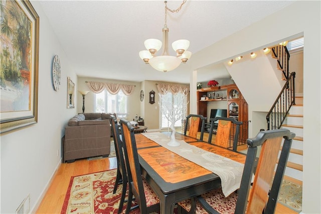 dining room with visible vents, baseboards, light wood finished floors, a notable chandelier, and stairs