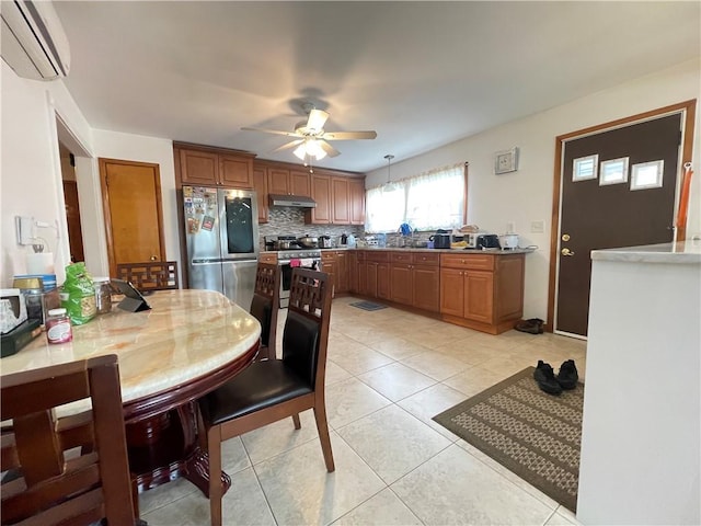 kitchen featuring a ceiling fan, brown cabinets, a wall mounted air conditioner, under cabinet range hood, and stainless steel appliances
