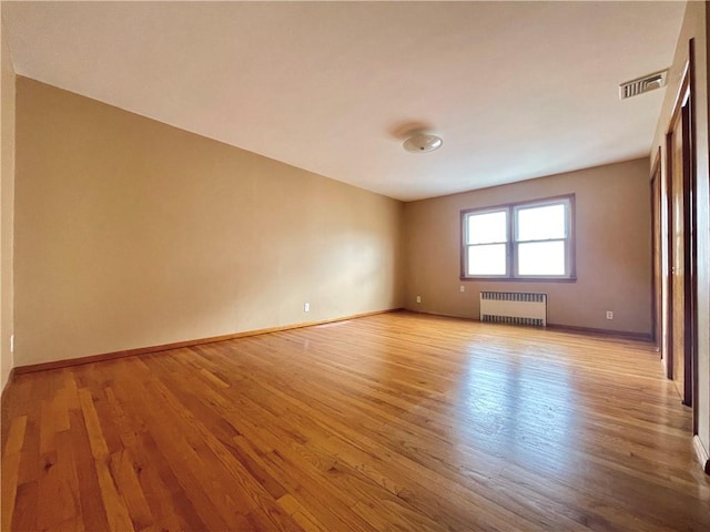 empty room with visible vents, light wood-style flooring, radiator, and baseboards