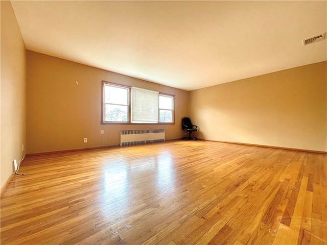unfurnished room featuring baseboards, visible vents, radiator heating unit, and light wood-style floors
