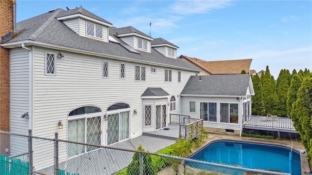 rear view of property featuring a fenced backyard, roof with shingles, a wooden deck, and a fenced in pool