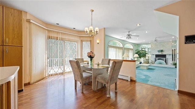dining space featuring light wood finished floors, a fireplace, ceiling fan with notable chandelier, and recessed lighting