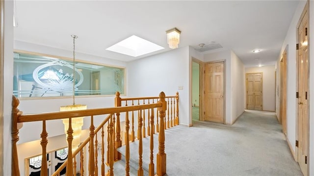 hall with light carpet, a skylight, baseboards, and an upstairs landing