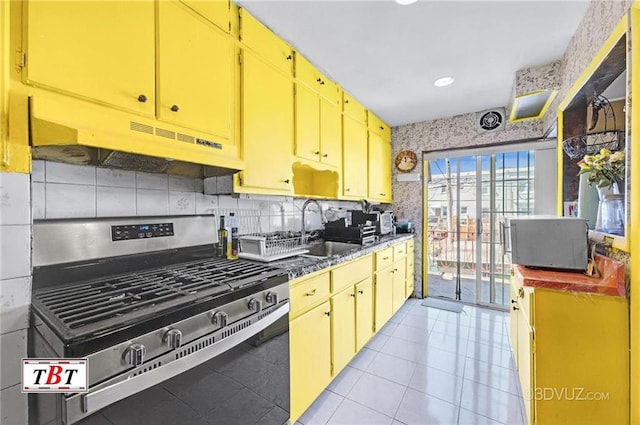 2052 E 28th St, Brooklyn, NY 11229 - kitchen with gas range, a sink, under cabinet range hood, backsplash, and yellow cabinetry