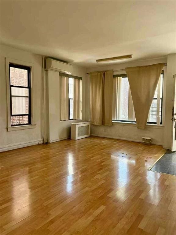 unfurnished room featuring baseboards, radiator heating unit, a wall mounted AC, and wood finished floors