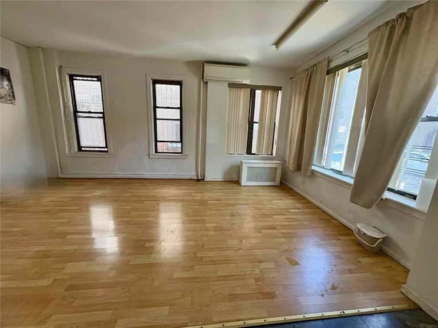 spare room featuring light wood finished floors, radiator, baseboards, and an AC wall unit