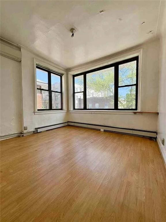 empty room with baseboards, a wall mounted AC, and wood finished floors