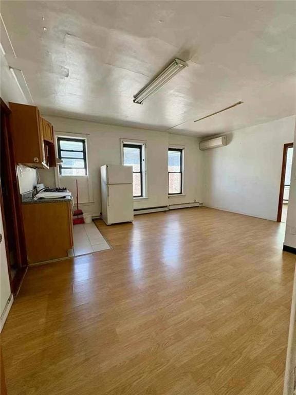 unfurnished living room featuring a wall mounted air conditioner, light wood-type flooring, and plenty of natural light