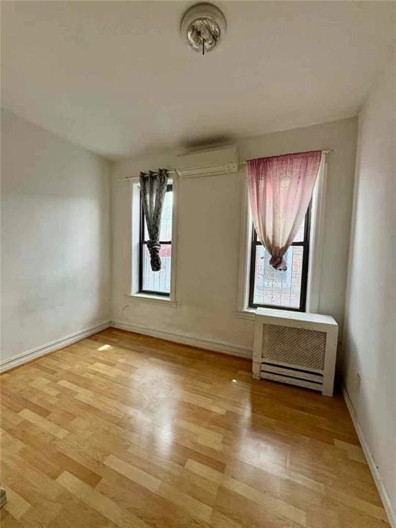 empty room with light wood-style flooring, a wall mounted AC, baseboards, and a healthy amount of sunlight